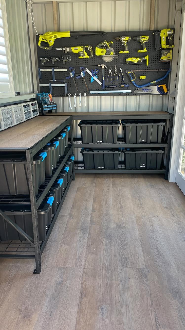 Power tools and hand tools hanging on a black pegboard above storage bins.