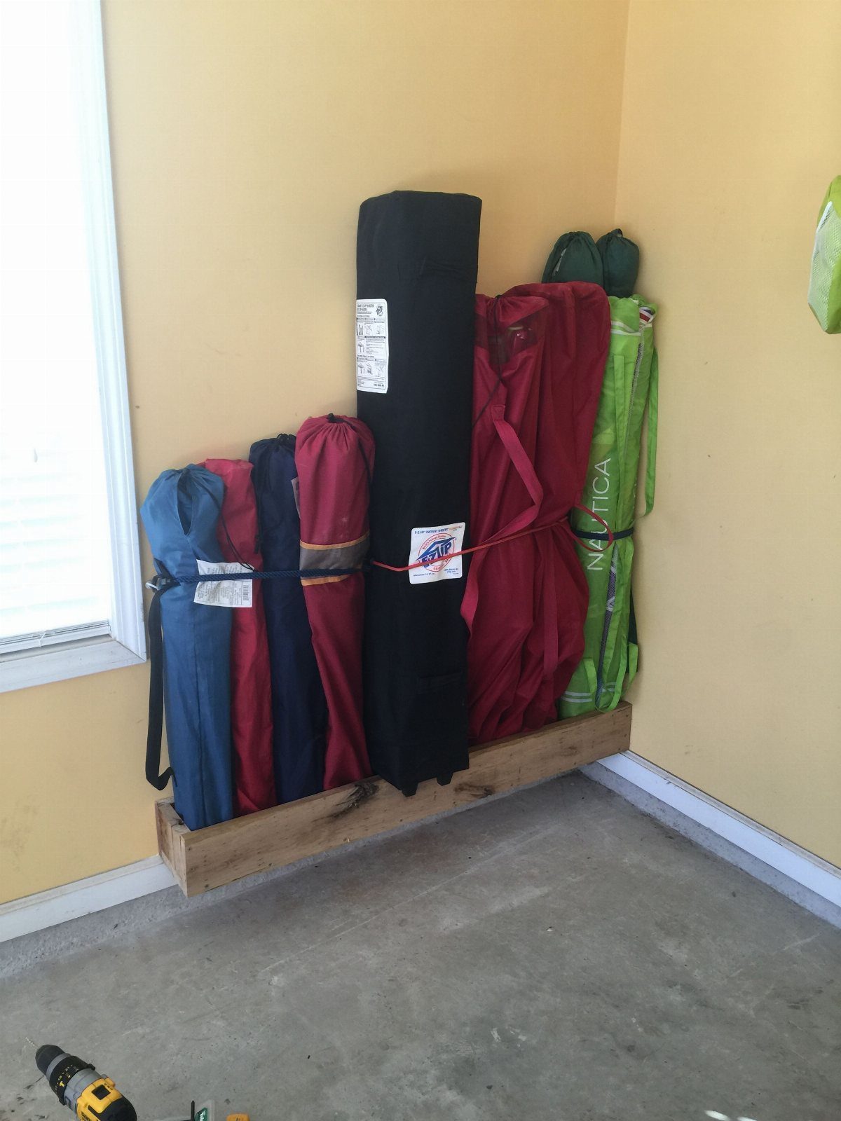 Garage Storage for 4 Camping Chair Ideas That Free the Floor 4 Rolled camping chairs secured by a bungee cord on a wooden wall-mounted shelf.