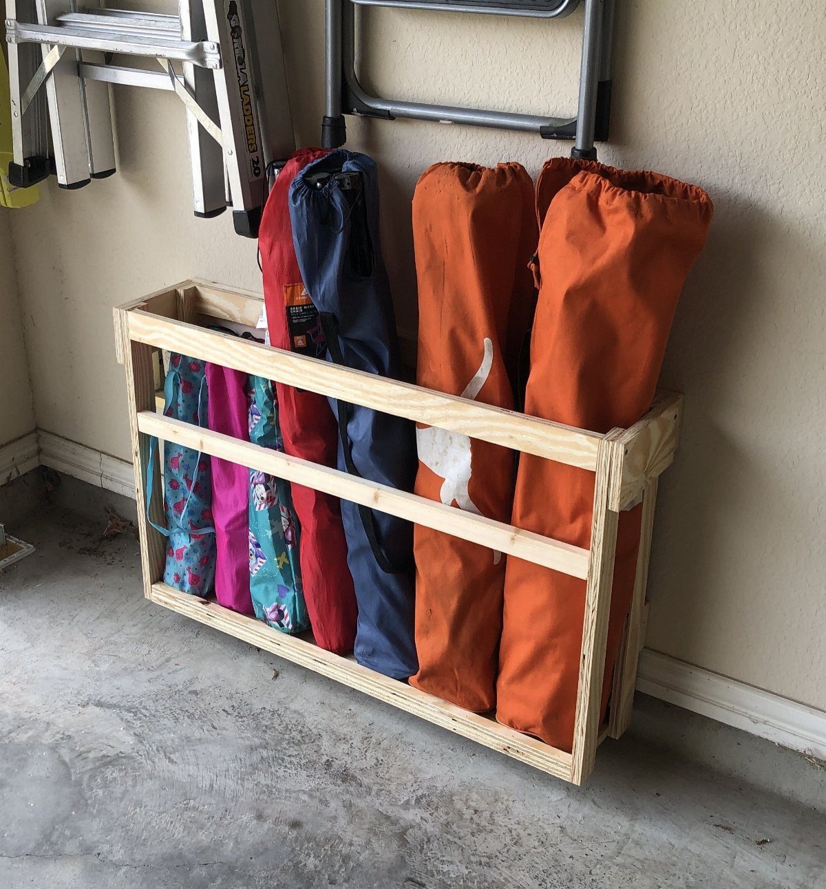 Garage Storage for 4 Camping Chair Ideas That Free the Floor 2 A wooden DIY 2x4 rack holding several folded camping chairs in colorful bags against a wall.
