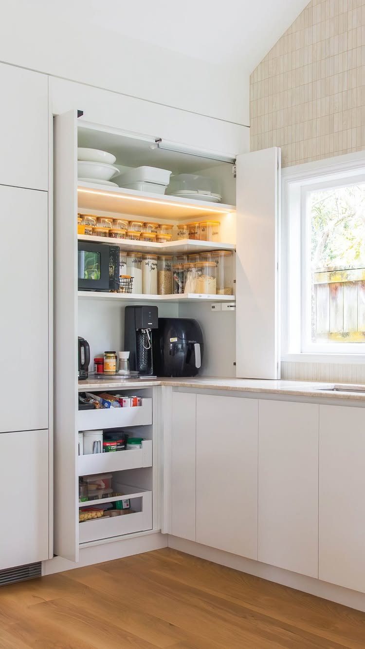 White kitchen cabinetry with open sliding doors revealing a pantry with appliances and food storage.