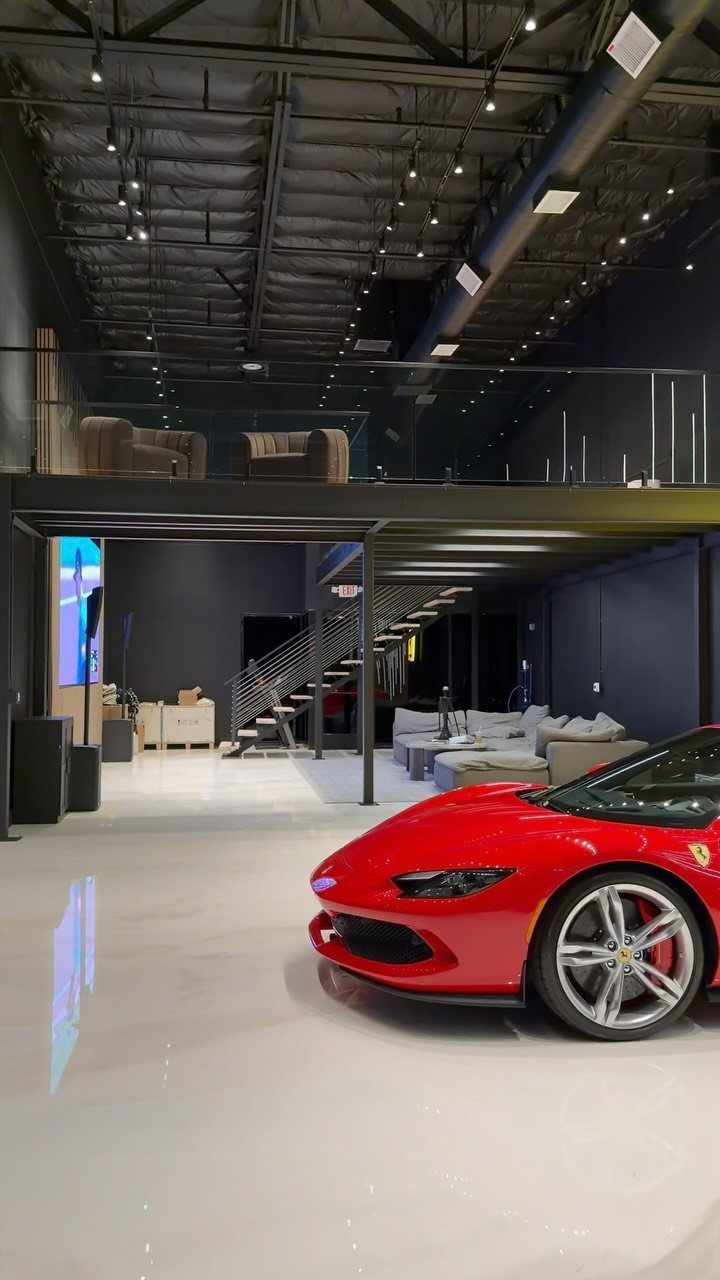 Red Ferrari parked in a luxury modern garage with a mezzanine living area and white floors.