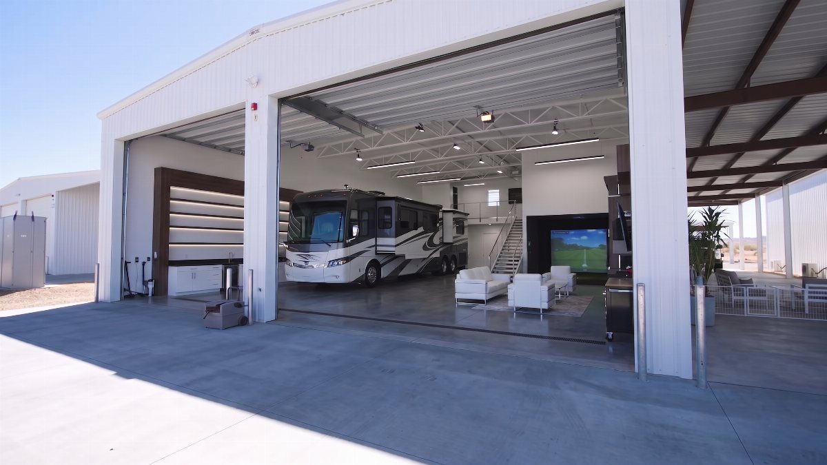 A luxury motorhome parked inside a large white metal garage with an integrated modern living room.