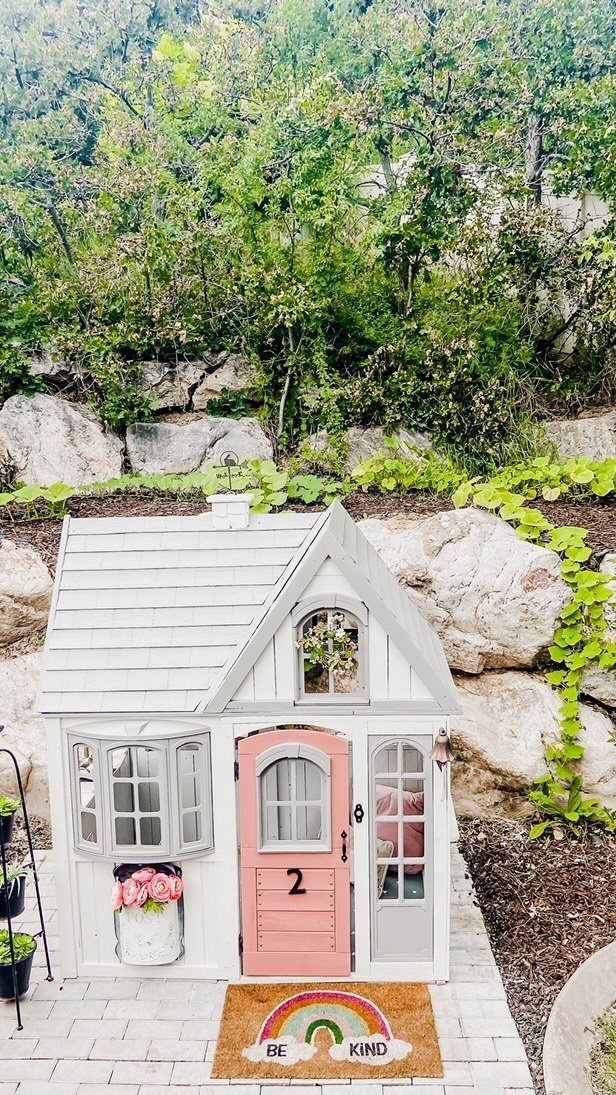 Garden Shed Design: 7 Ways to Use the Space You Have 3 A small white wooden playhouse with a pink door and decorative windows on a patio.