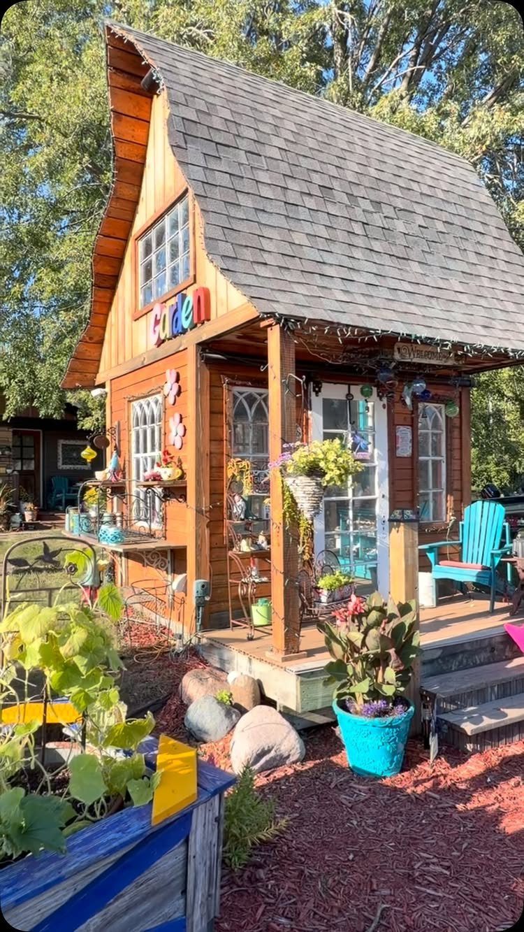 Garden Shed Design: 7 Ways to Use the Space You Have 1 A whimsical wooden garden shed with a curved roof, decorated porch, and colorful potted plants.