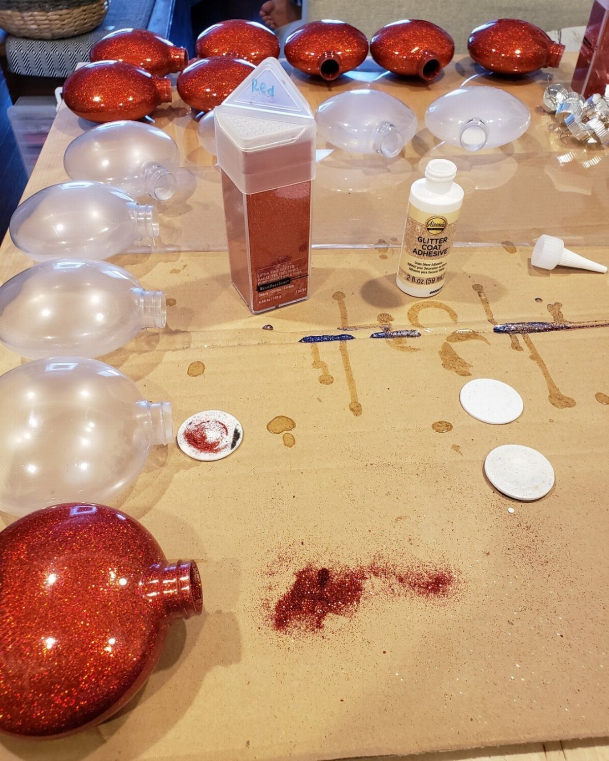 Glitter DIY Ornaments to Make 5 Ways 1 Red and clear glittery plastic ornaments scattered on a brown paper workspace with glue and glitter.