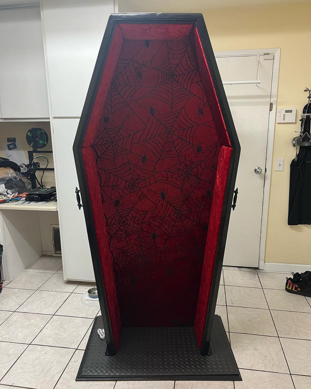 5 Goth Halloween Decor Ideas for a Properly Dark Holiday 4 An open black coffin with red spiderweb patterned velvet lining standing on a tiled floor.
