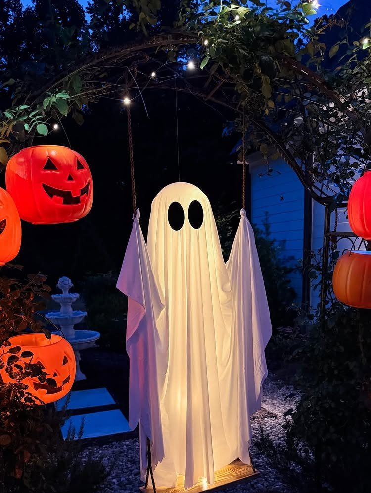 5 Goth Halloween Decor Ideas for a Properly Dark Holiday 2 A glowing white ghost figure stands among illuminated orange jack-o'-lanterns in a dark garden.