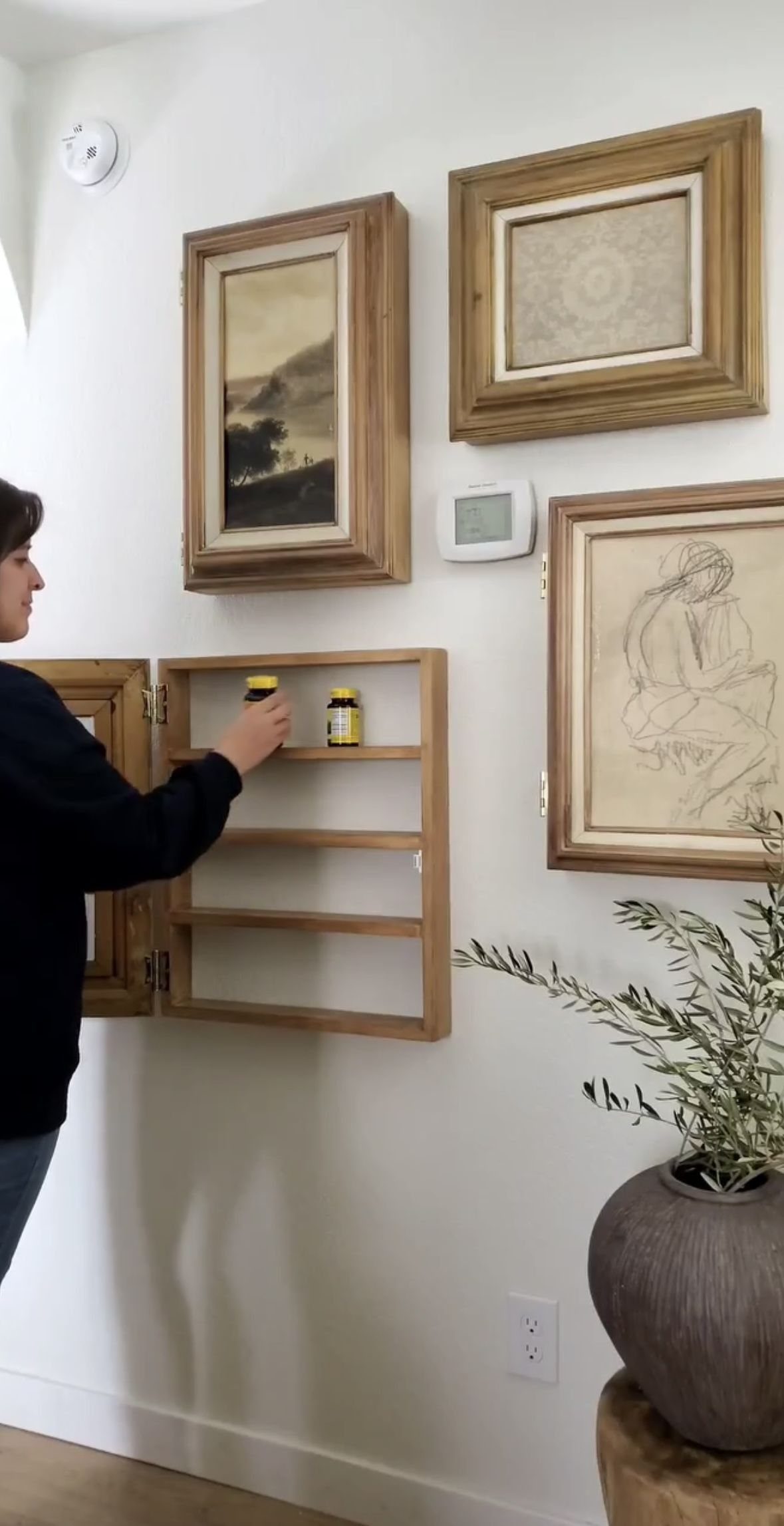 Hidden Storage for Picture Frame: 5 Smart DIY Projects 5 A woman opens a wooden picture frame to reveal a hidden storage shelf with small bottles.