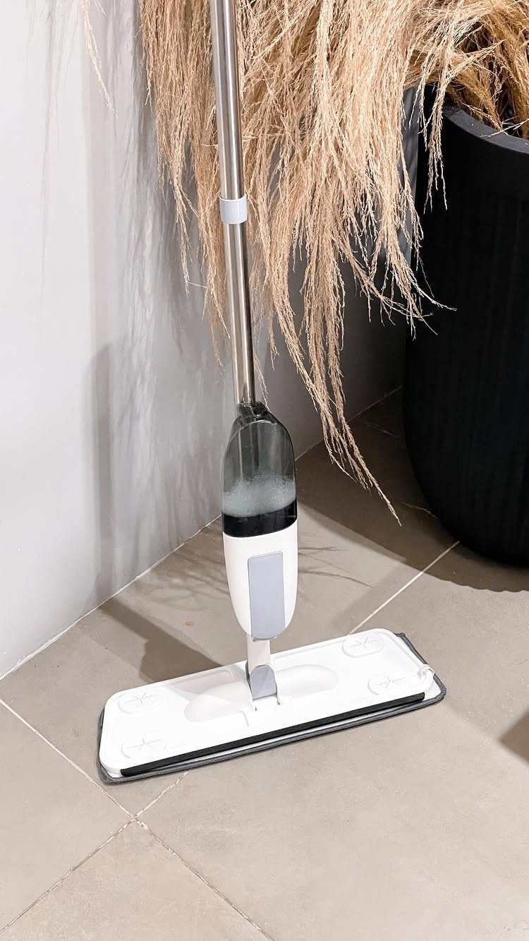 A white spray mop resting on a tiled floor next to a large black planter.