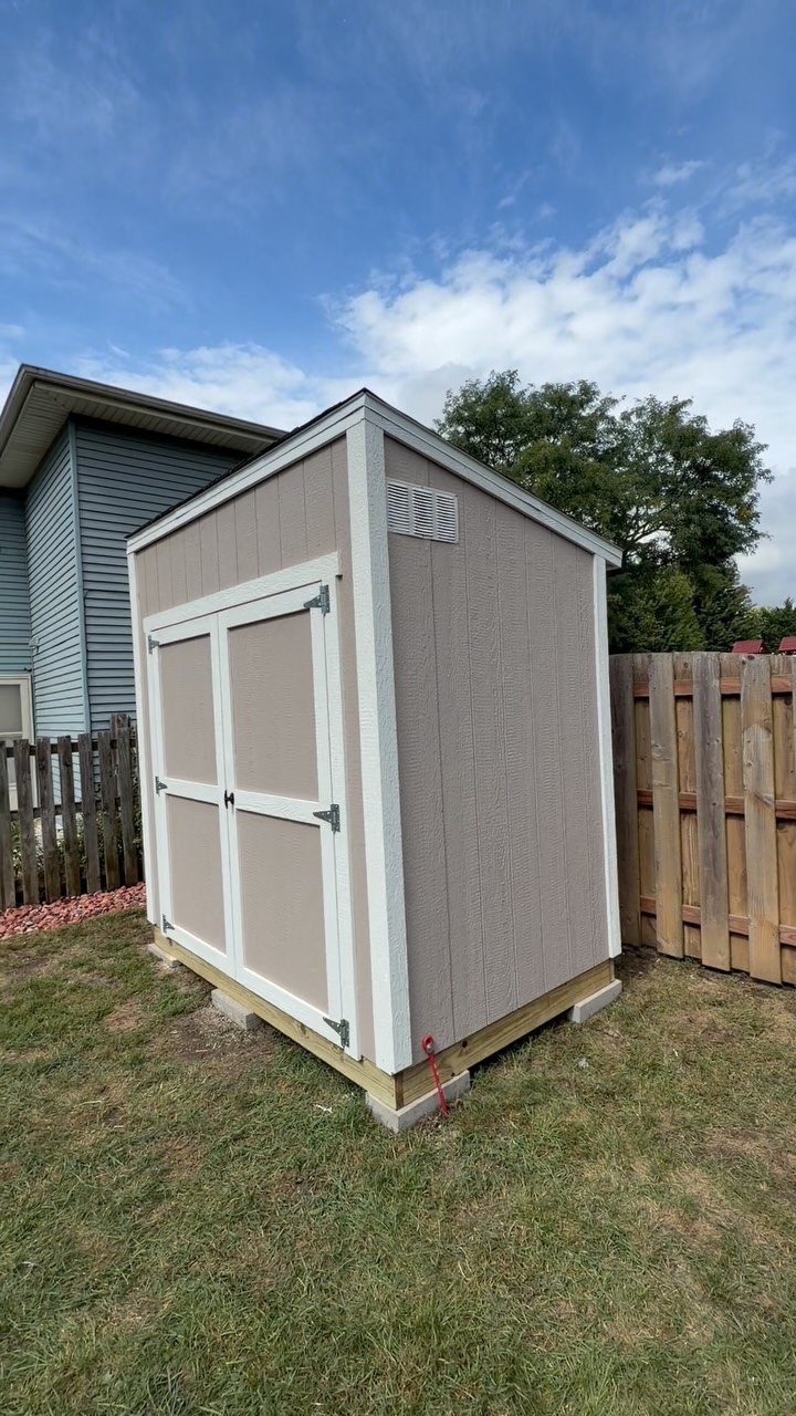 8 Lean-To Shed Ideas for Storage, Parking and Backyard Layouts 8 A small tan lean-to shed with white trim sits on a green lawn next to a fence.
