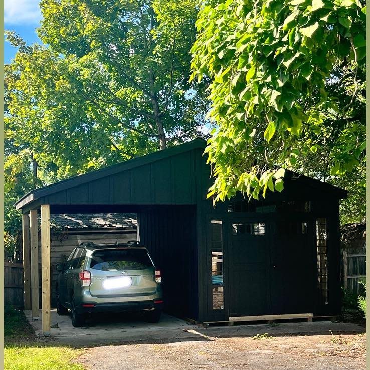 8 Lean-To Shed Ideas for Storage, Parking and Backyard Layouts 7 A black wooden lean-to shed sheltering a silver SUV parked under green trees.