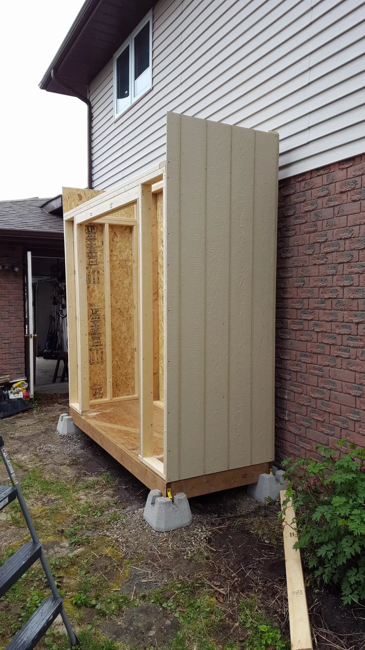 8 Lean-To Shed Ideas for Storage, Parking and Backyard Layouts 5 Wooden frame of a lean-to shed under construction against a house wall.