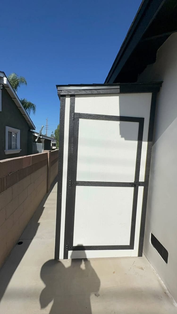 8 Lean-To Shed Ideas for Storage, Parking and Backyard Layouts 6 A white lean-to shed with dark trim stands in a narrow outdoor walkway.