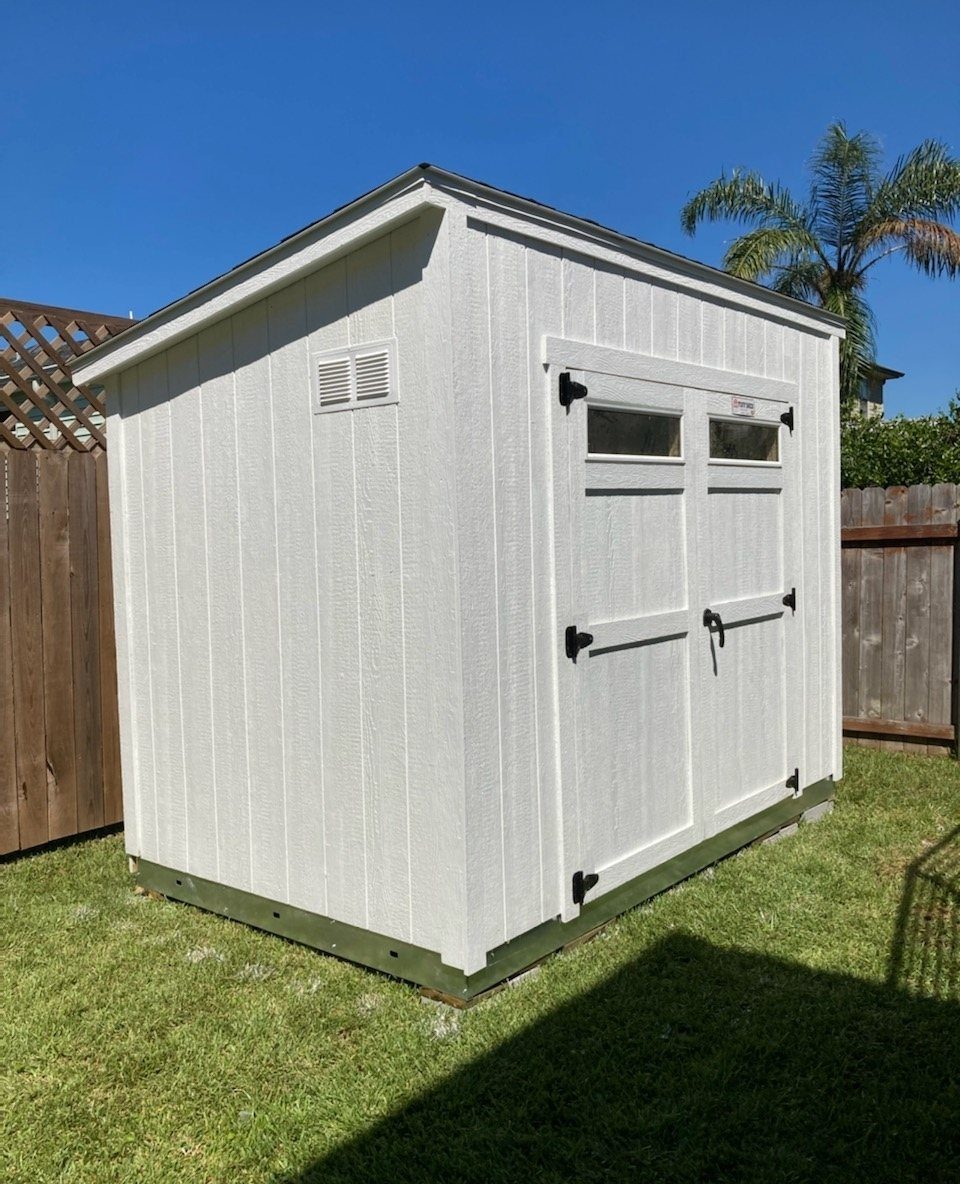 8 Lean-To Shed Ideas for Storage, Parking and Backyard Layouts 2 A white wooden lean-to shed with double doors and small windows on a green lawn.