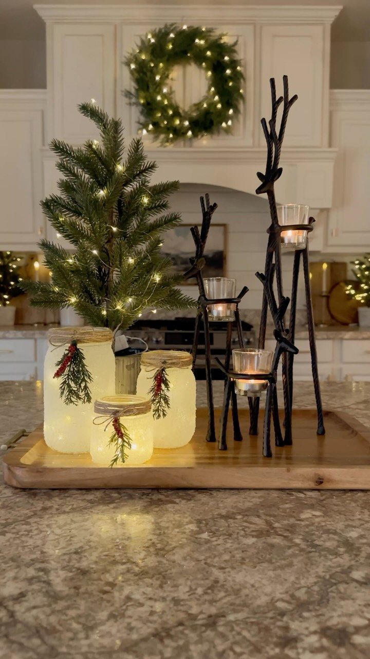 Frosted mason jars glowing with fairy lights arranged on a wooden tray with a small Christmas tree.
