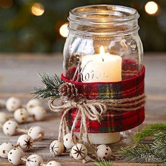 A lit candle inside a mason jar decorated with plaid fabric, twine, and a pinecone.