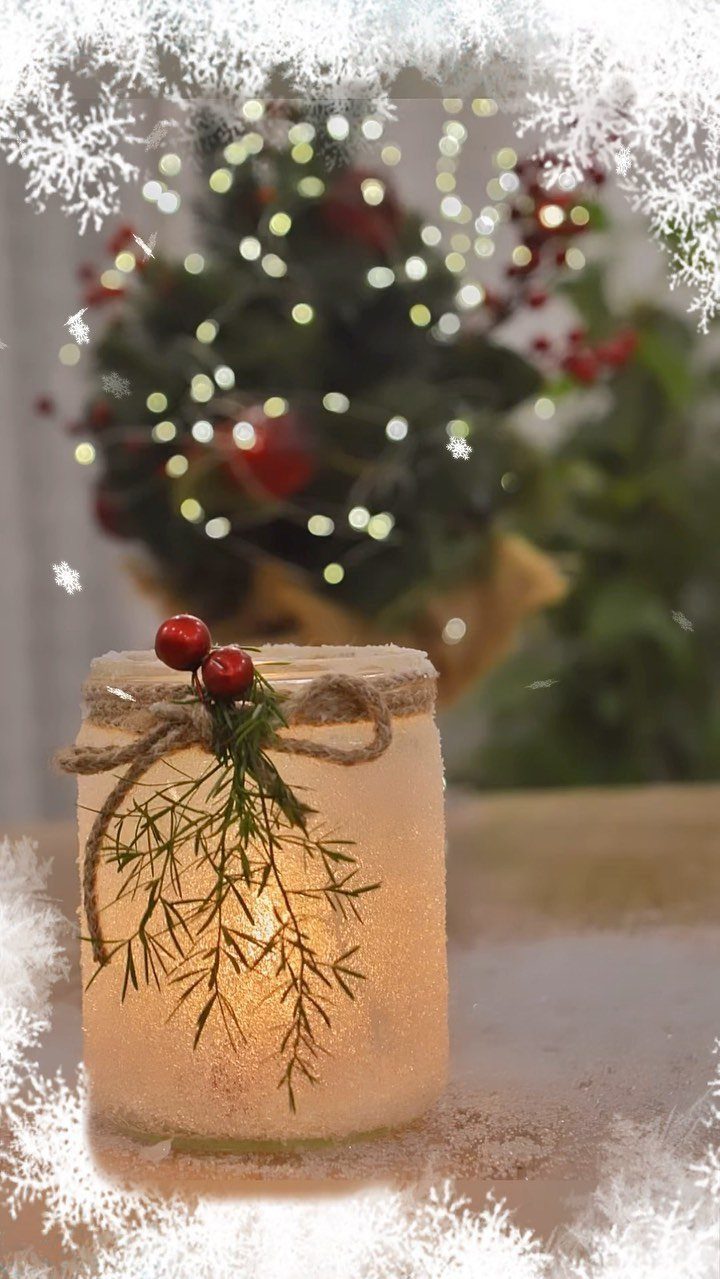 A glowing frosted mason jar decorated with twine, greenery, and red berries on a wooden surface.