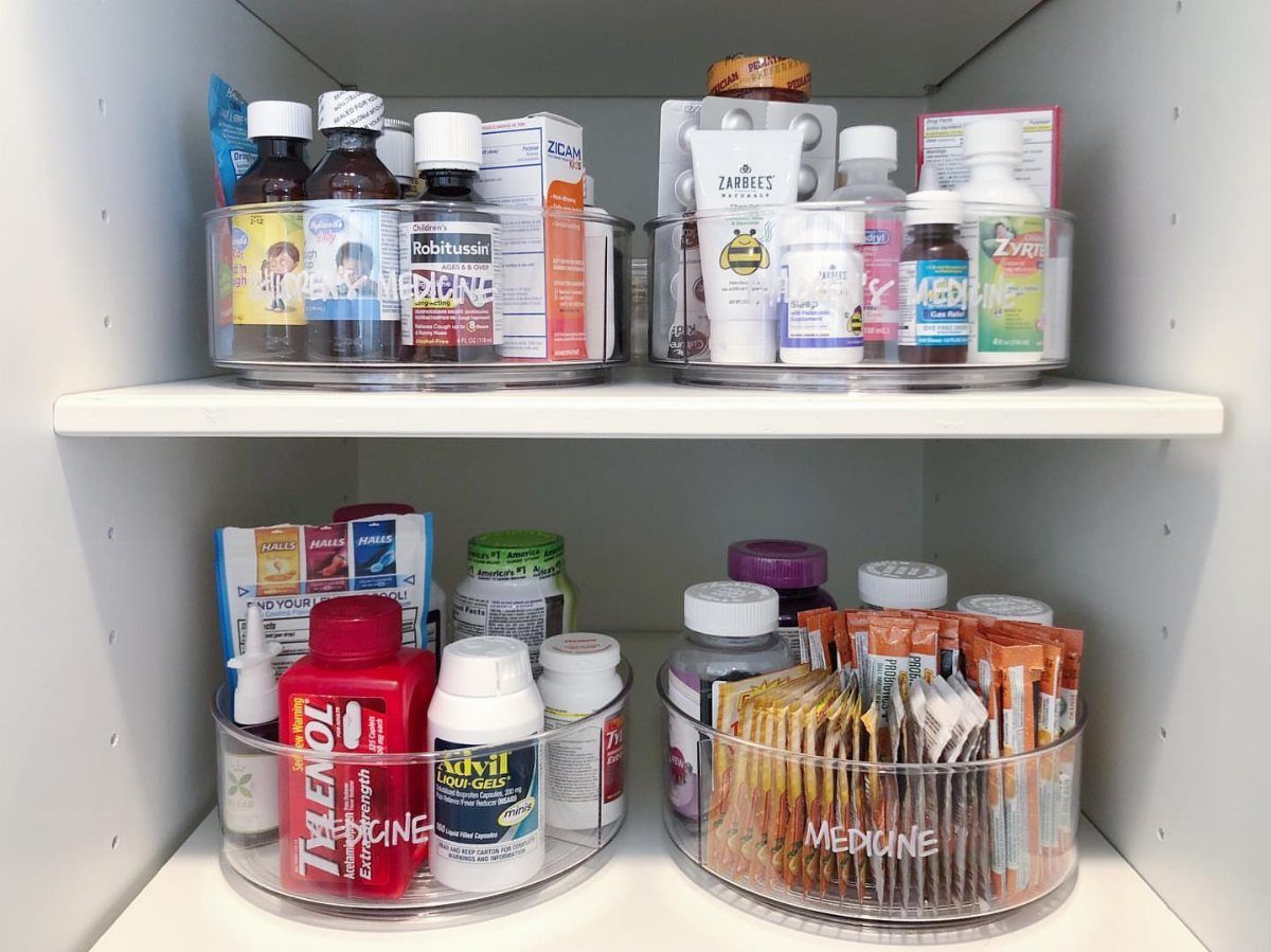 Medicine Cabinet Organization: 5 Fixes to Try in 2026 4 Clear acrylic rotating trays filled with various medicine bottles and packets on white shelves.