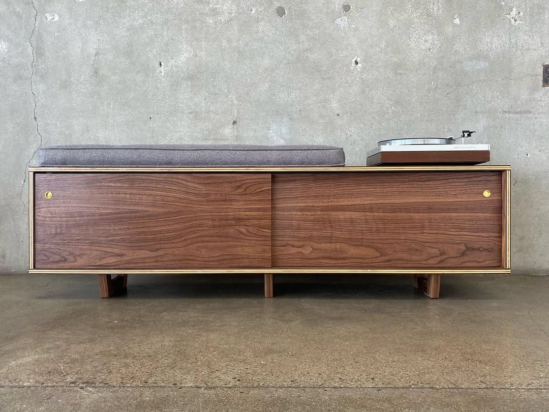 Mid Century Modern Entryway Bench With Storage: 8 Ideas 3 A long mid-century modern wooden bench with a grey cushion against a concrete wall.