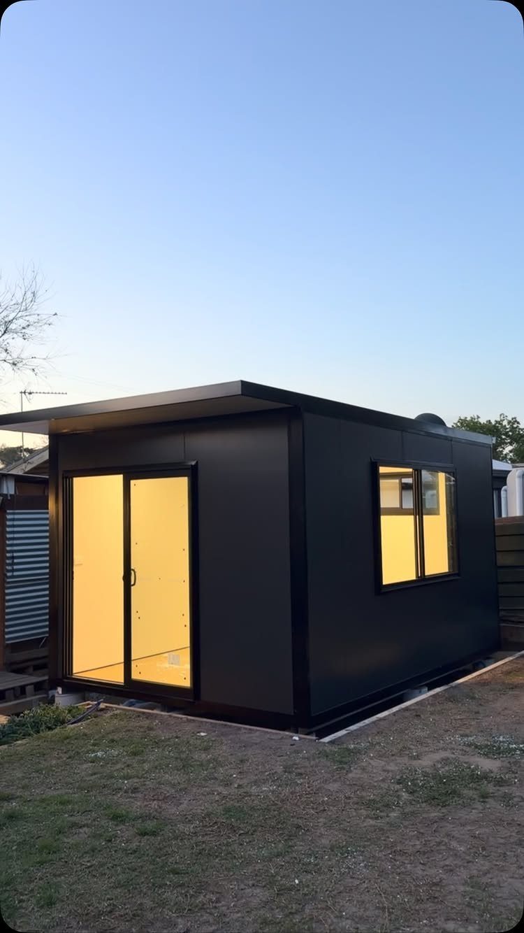 7 Modern Shed Ideas for Compact Yards, Studios & Integrated Outdoor Living 5 A modern black prefab garden pod with glass doors and a window on a lawn.