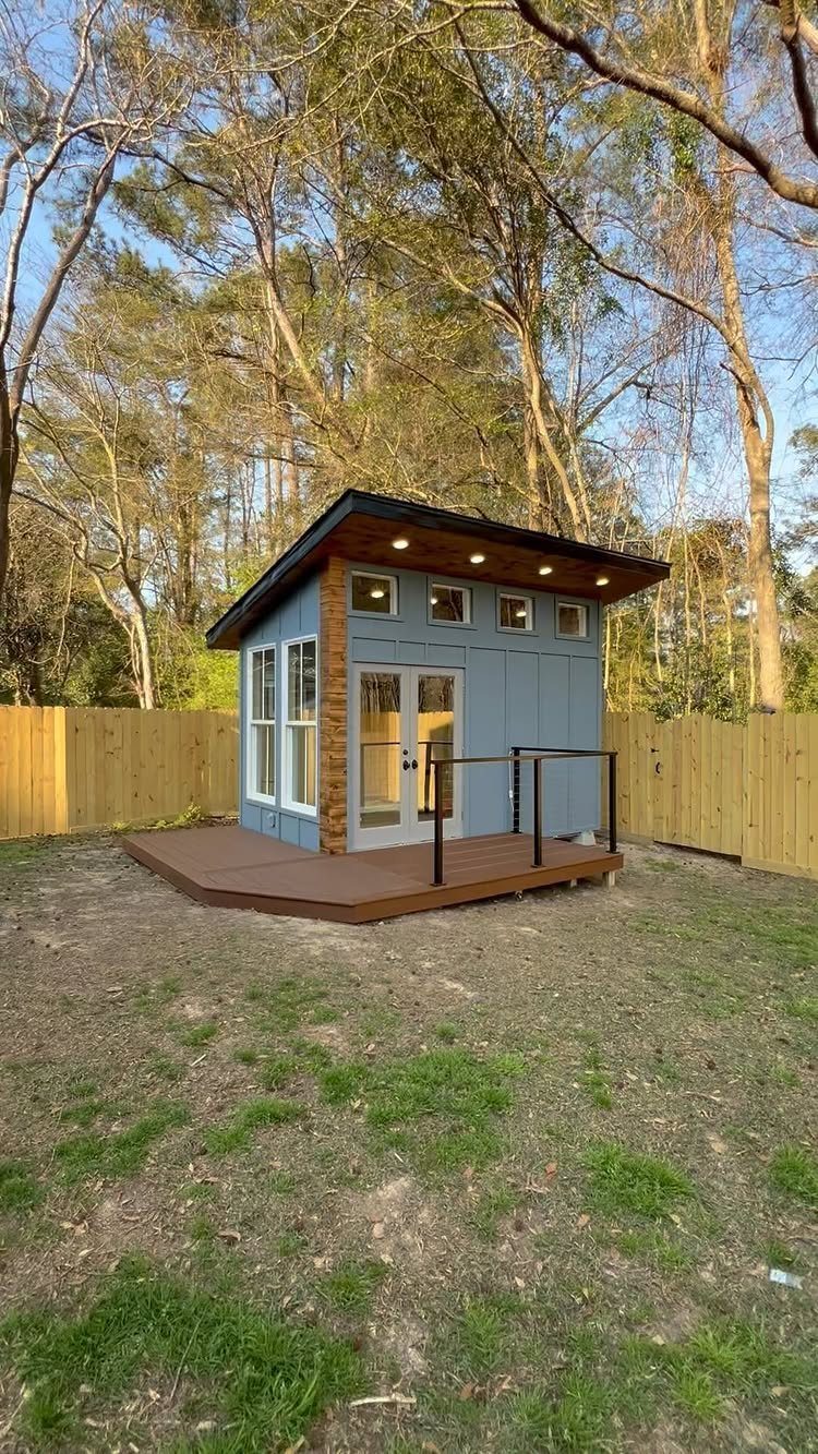7 Modern Shed Ideas for Compact Yards, Studios & Integrated Outdoor Living 1 A small modern blue shed with a slanted roof on a wooden deck in a yard.