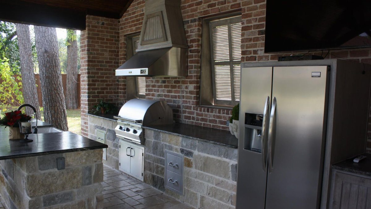 5 Outdoor Kitchen Fridge Ideas for Your Patio Setup 5 Stainless steel outdoor kitchen with a built-in grill, stone countertops, and a large refrigerator.