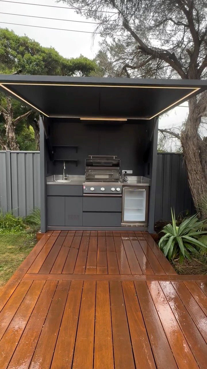 5 Outdoor Kitchen Fridge Ideas for Your Patio Setup 1 A modern outdoor kitchen setup with a grill, sink, and mini fridge on a wooden deck.