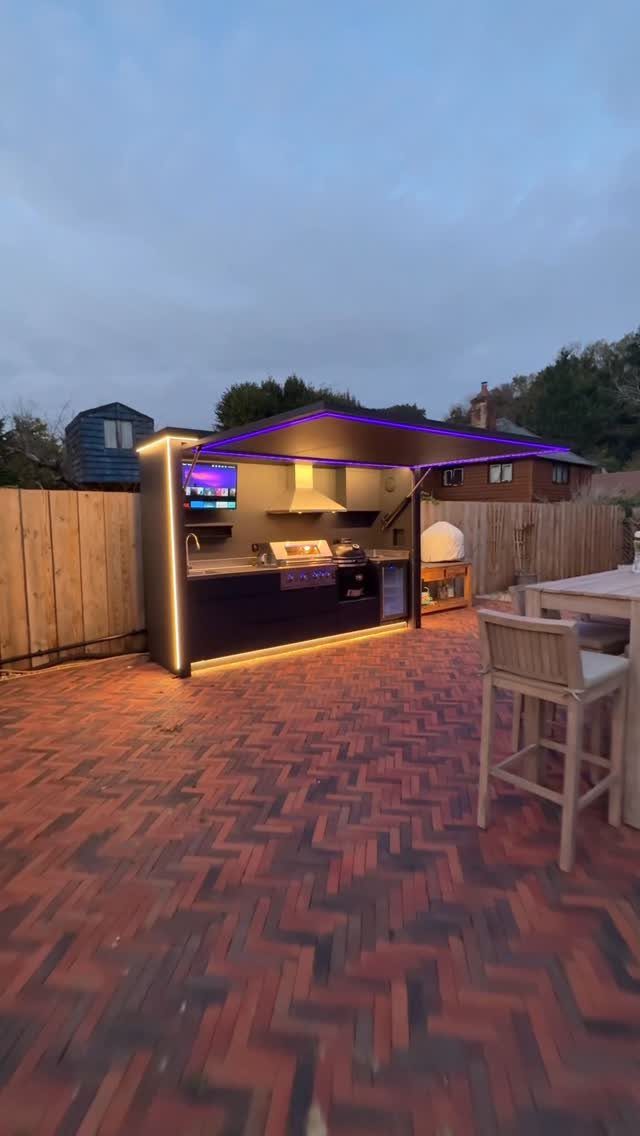 5 Outdoor Kitchen Fridge Ideas for Your Patio Setup 3 Outdoor kitchen with a built-in grill, television, and under-counter refrigerator under a lit canopy.