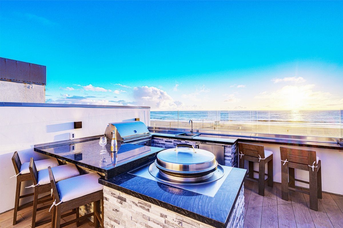 7 Outdoor Patio Kitchen Ideas for Every Backyard Style 6 Outdoor rooftop kitchen with black countertops and stainless steel appliances overlooking the bright blue ocean.