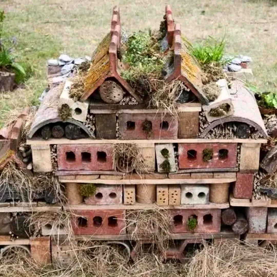 A rustic insect hotel constructed from bricks, tiles, and wood pieces in a garden.