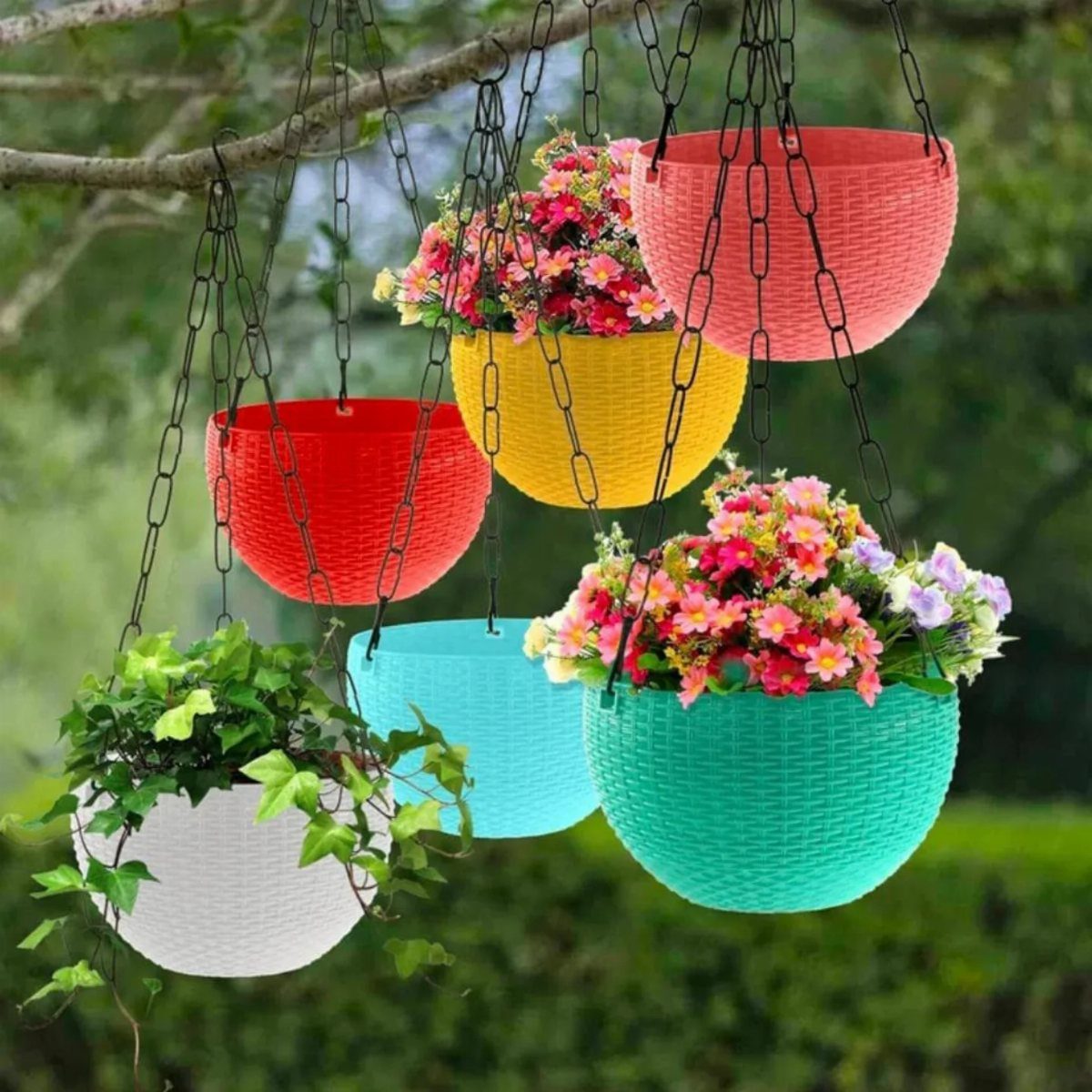 Colorful hanging flower baskets suspended from tree branches by black chains in a garden.