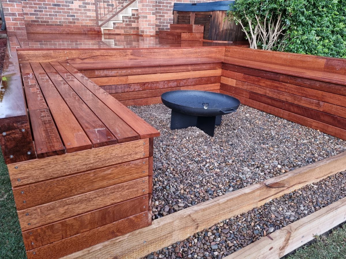 28 Outdoor Wooden Deck Ideas for Any Yard Size 21 Reddish-brown wooden bench surrounding a black metal fire bowl on a gravel surface.