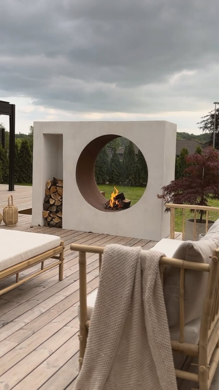 28 Outdoor Wooden Deck Ideas for Any Yard Size 27 A modern white circular outdoor fireplace burning on a wooden deck with lounge furniture.