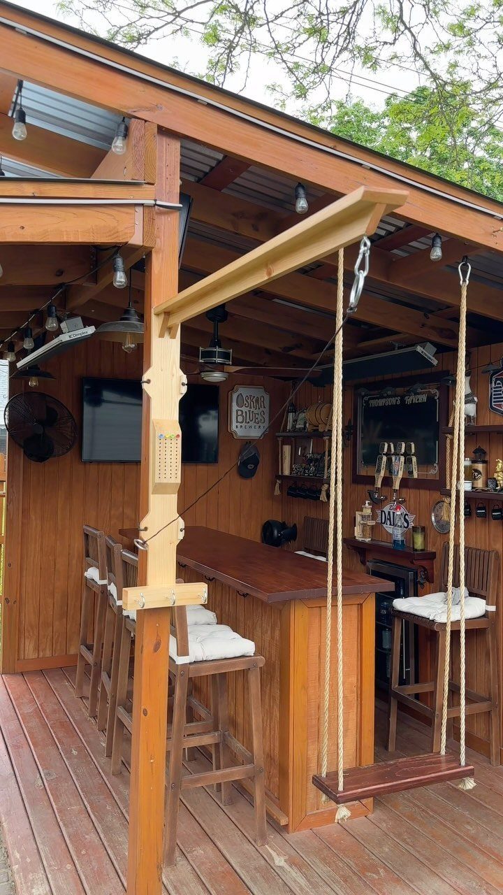 28 Outdoor Wooden Deck Ideas for Any Yard Size 9 Wooden swing hanging from a beam in a covered outdoor bar area on a deck.