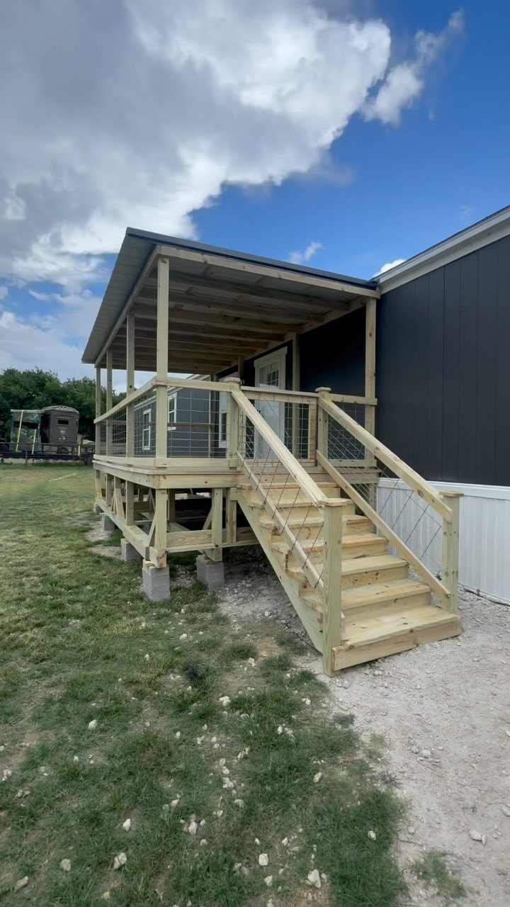 28 Outdoor Wooden Deck Ideas for Any Yard Size 25 Wooden deck with stairs and cable railings attached to a dark grey building under a cloudy sky.