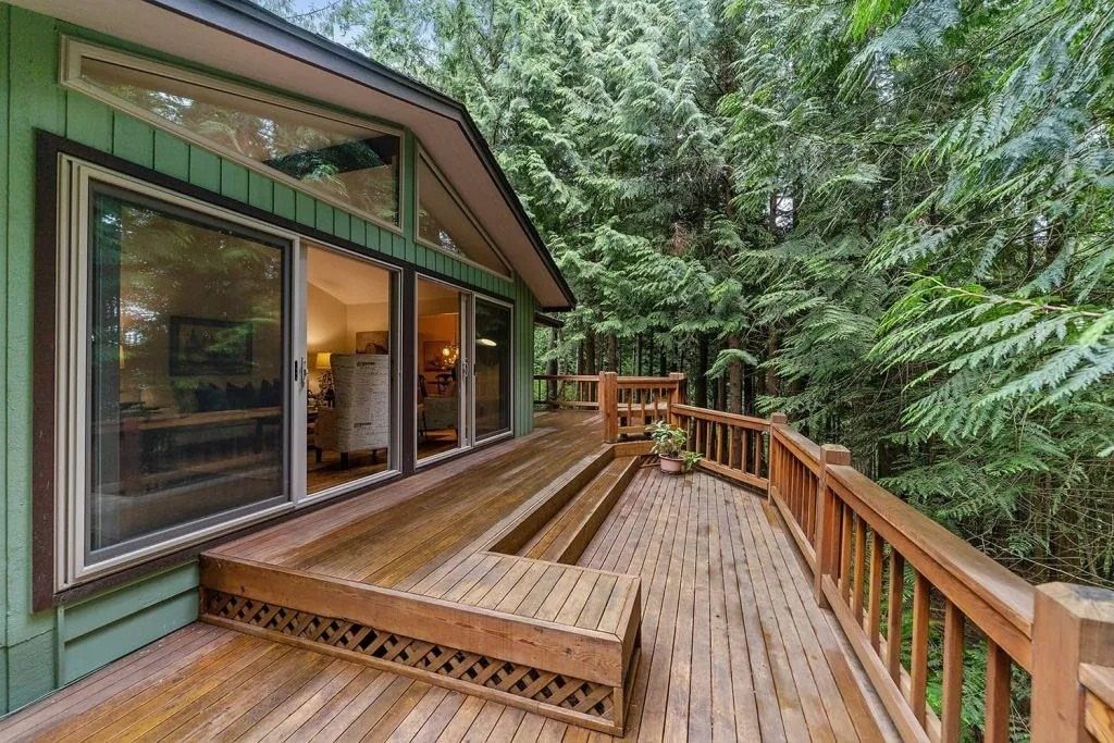 28 Outdoor Wooden Deck Ideas for Any Yard Size 2 A multi-level wooden deck with railings overlooking a lush green forest next to a house.