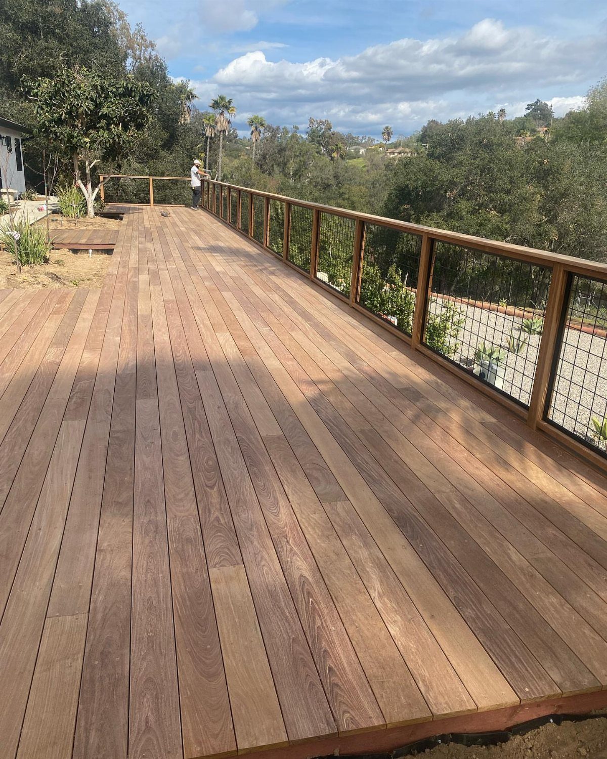 28 Outdoor Wooden Deck Ideas for Any Yard Size 19 A wide wooden deck with natural grain texture overlooking a green hillside and cloudy sky.