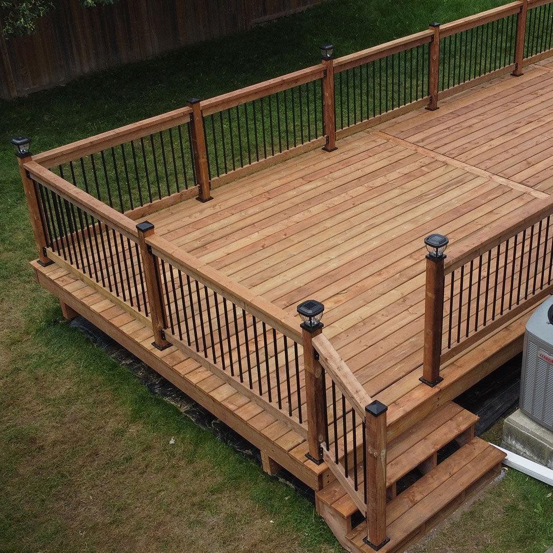 28 Outdoor Wooden Deck Ideas for Any Yard Size 16 A large wooden platform deck with black metal railings and steps leading to a lawn.