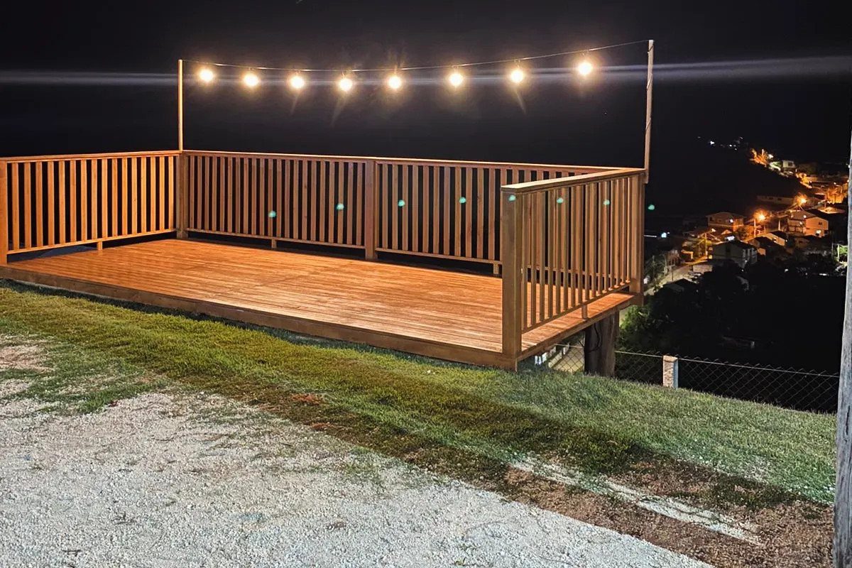 28 Outdoor Wooden Deck Ideas for Any Yard Size 15 A wooden raised deck with railings and string lights overlooking a city at night.