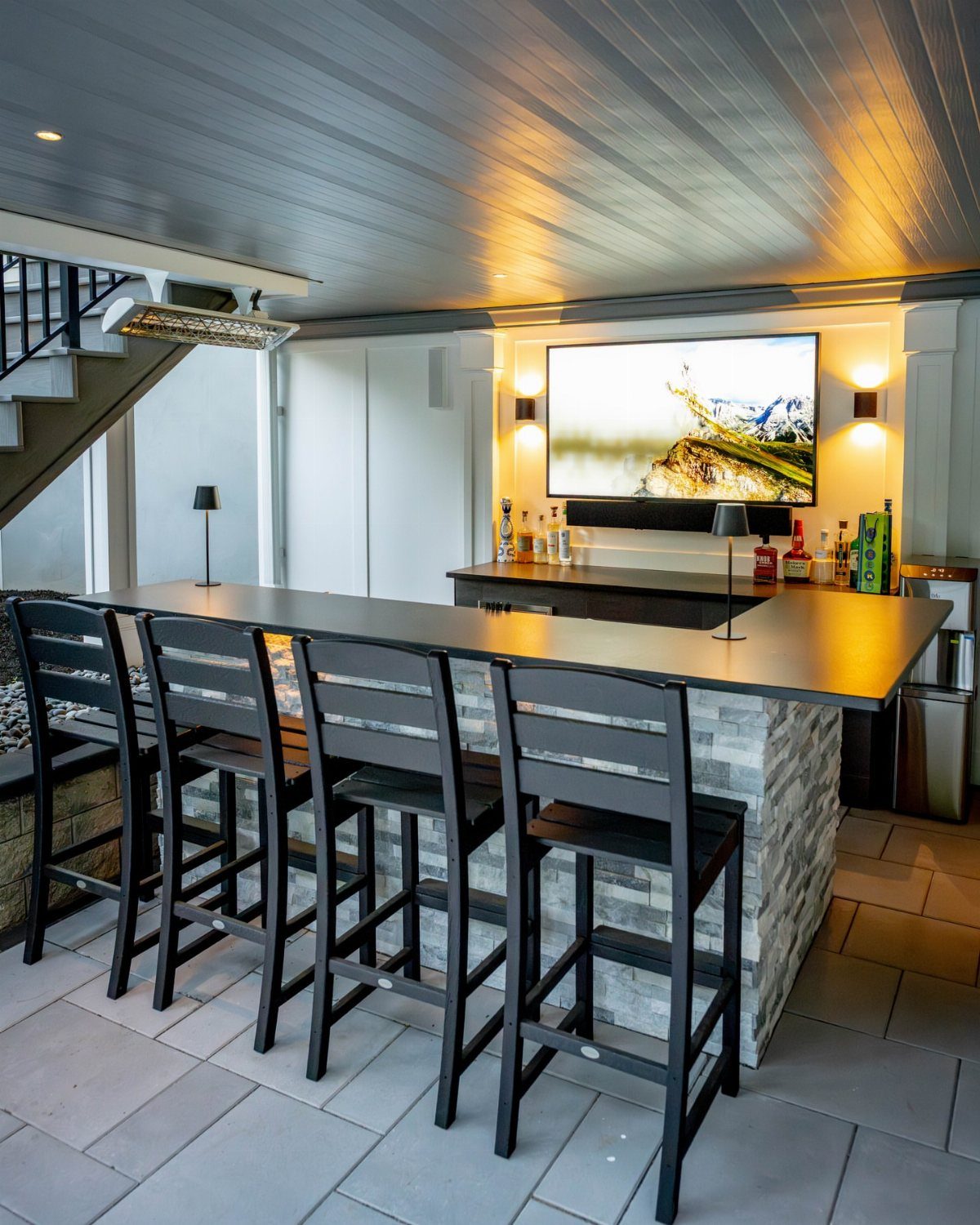 20 Patio and Deck Ideas to Make Your Yard Feel Like a Room 6 A modern outdoor bar with a black countertop, stone base, and four black bar stools.