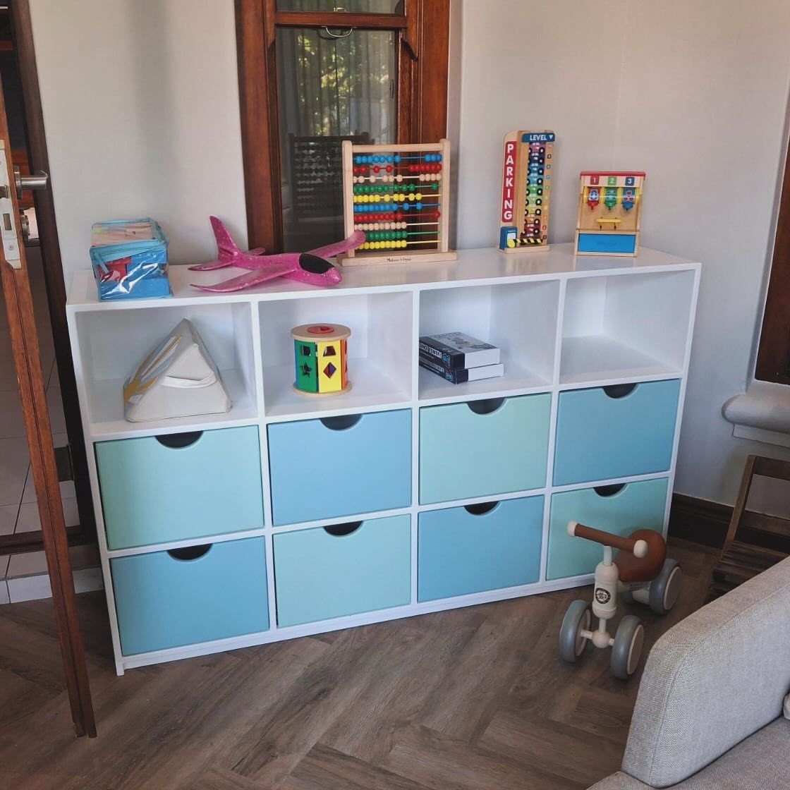 White cube storage unit with light blue fabric drawers containing various colorful children's toys.