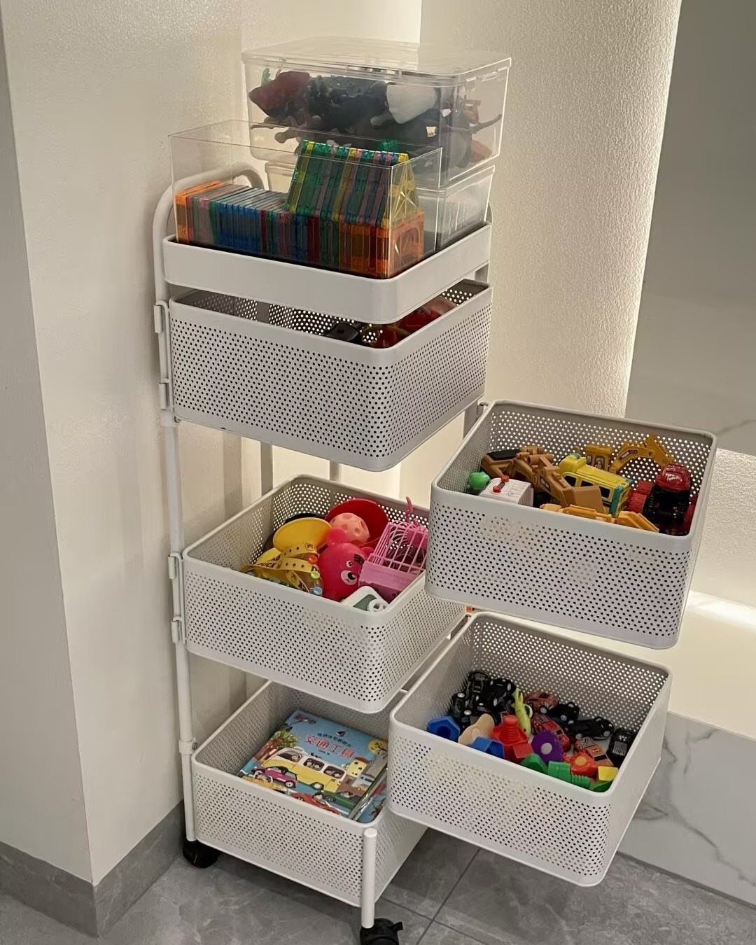 White rolling storage cart with perforated baskets filled with colorful children's toys and books.