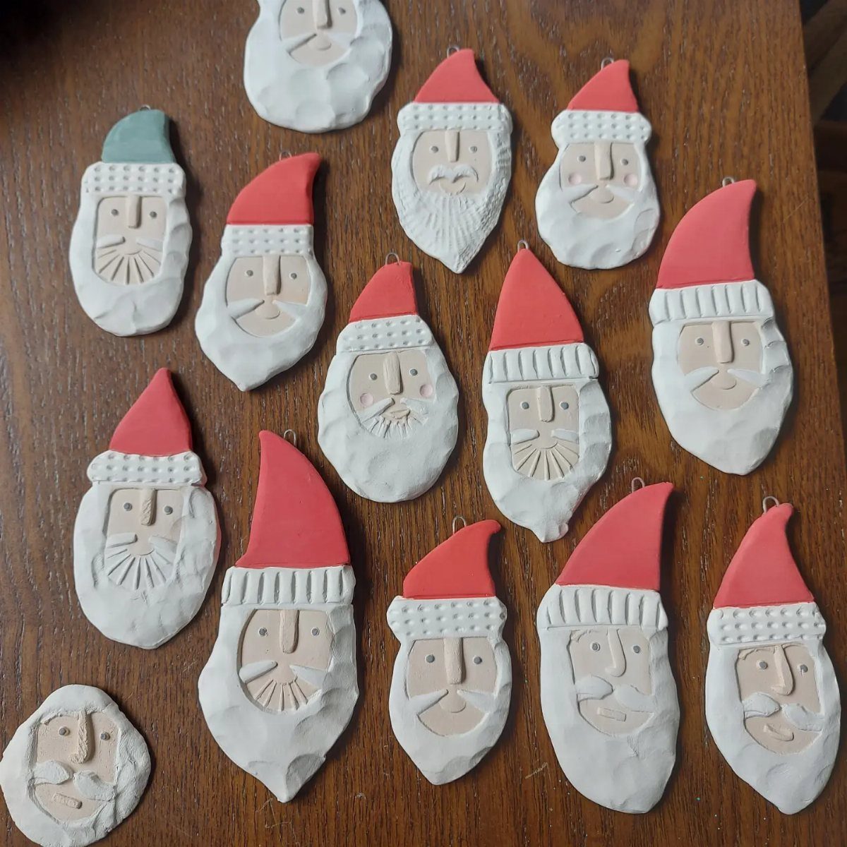 8 Red and Green Christmas Tree Ideas 5 Handmade clay Santa Claus face ornaments with red and teal hats on a wooden surface.