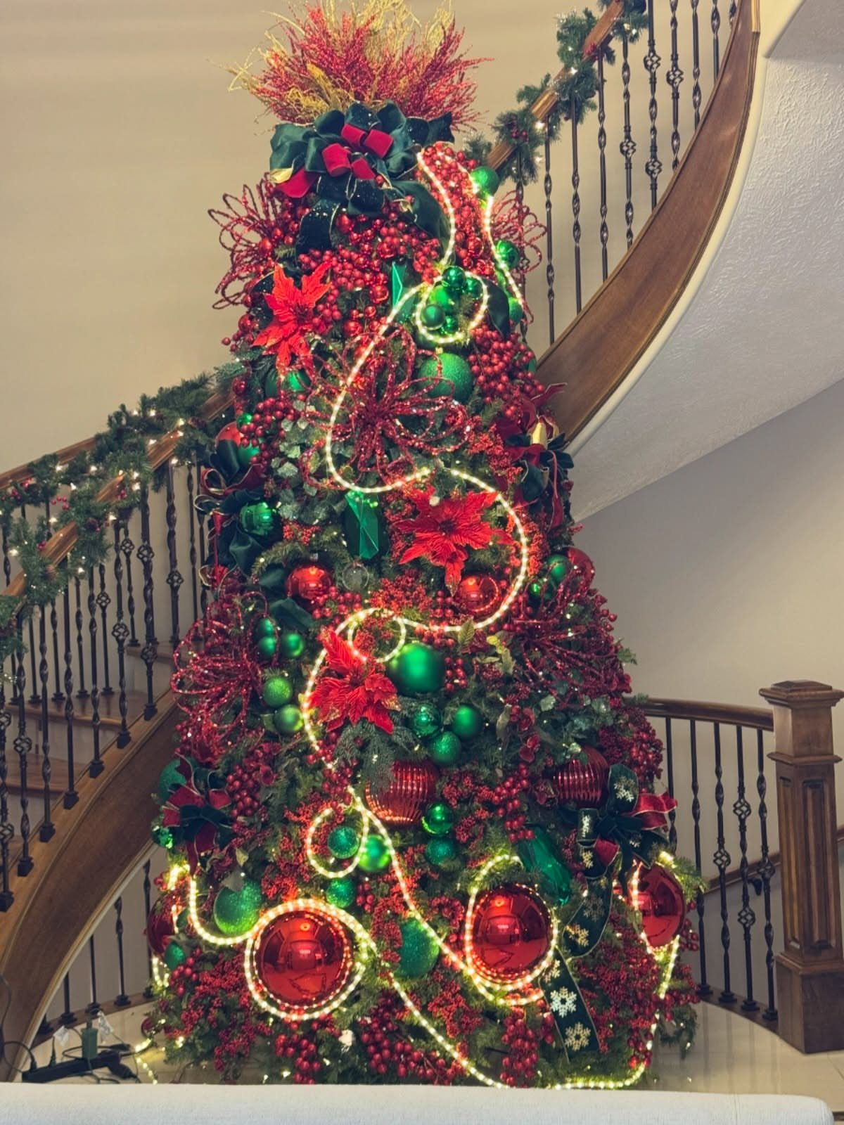 8 Red and Green Christmas Tree Ideas 3 A decorated Christmas tree with red and green ornaments and lights next to a staircase.