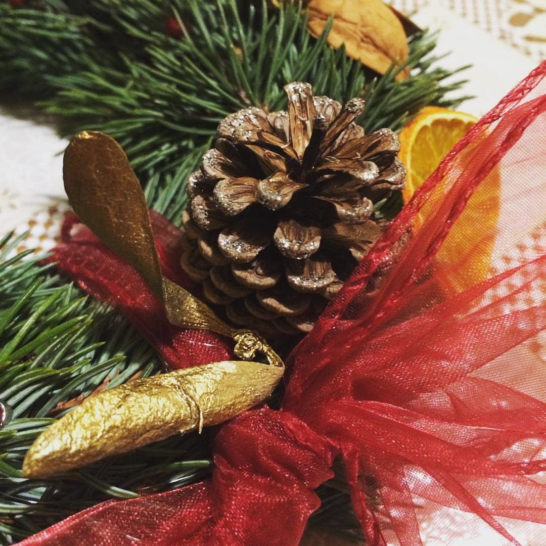 8 Red and Green Christmas Tree Ideas 6 A brown pinecone nestled among green pine needles with red ribbon and dried orange slices.