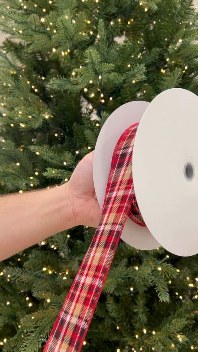 8 Red and Green Christmas Tree Ideas 2 A hand holding a spool of red plaid ribbon in front of a lit Christmas tree.