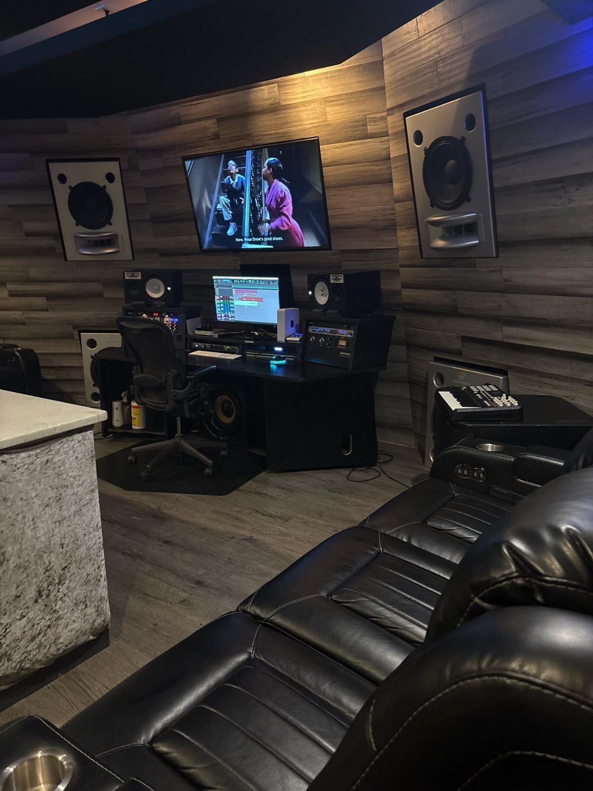 5 Room on Top of Garage Ideas for Extra Living Space 4 Music production studio with desk, monitors, and wood-paneled walls next to a black leather sofa.