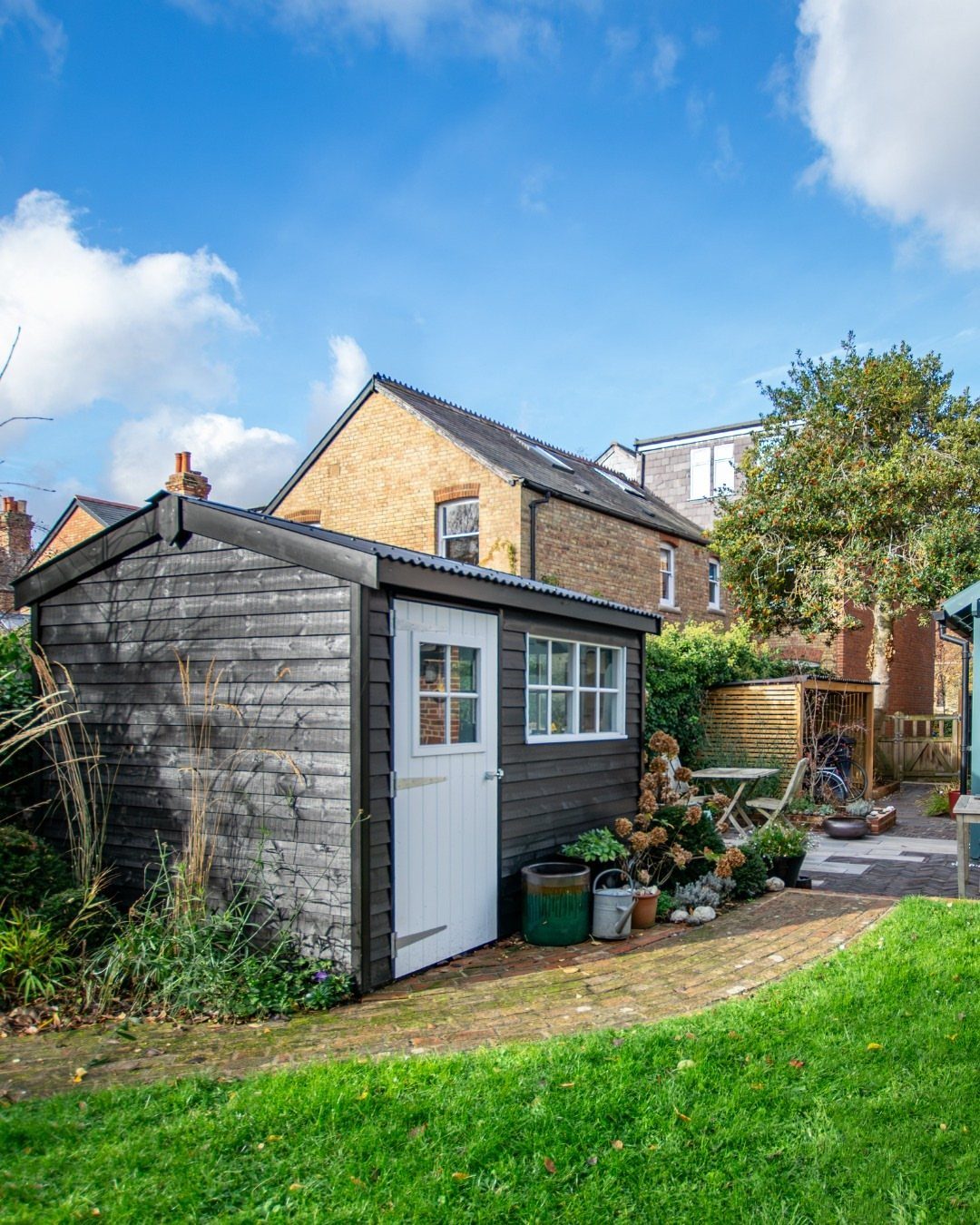 10 Shed Colors Ideas to Paint Your Backyard Storage 10 A dark gray wooden garden shed featuring a bright white door and window frames.