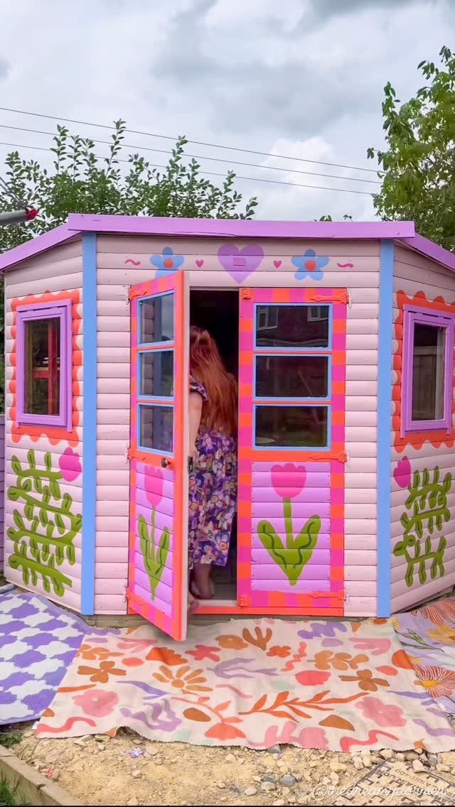 10 Shed Colors Ideas to Paint Your Backyard Storage 4 A brightly painted pink and purple wooden playhouse with colorful floral decorations outdoors.