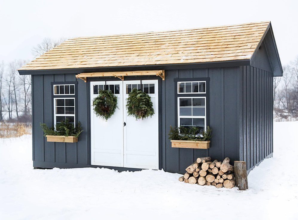 10 Shed Colors Ideas to Paint Your Backyard Storage 1 Charcoal gray wooden shed with white doors and windows sitting in a snowy field.